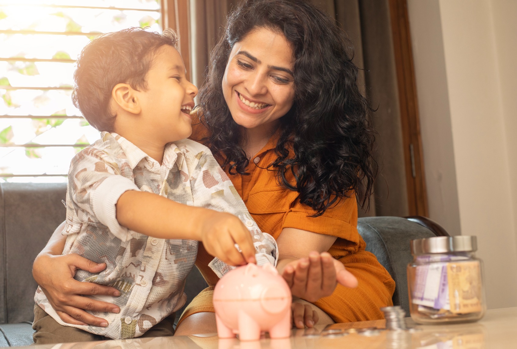 Mother and son saving coins in piggy bank at home (Getty Images/triloks)