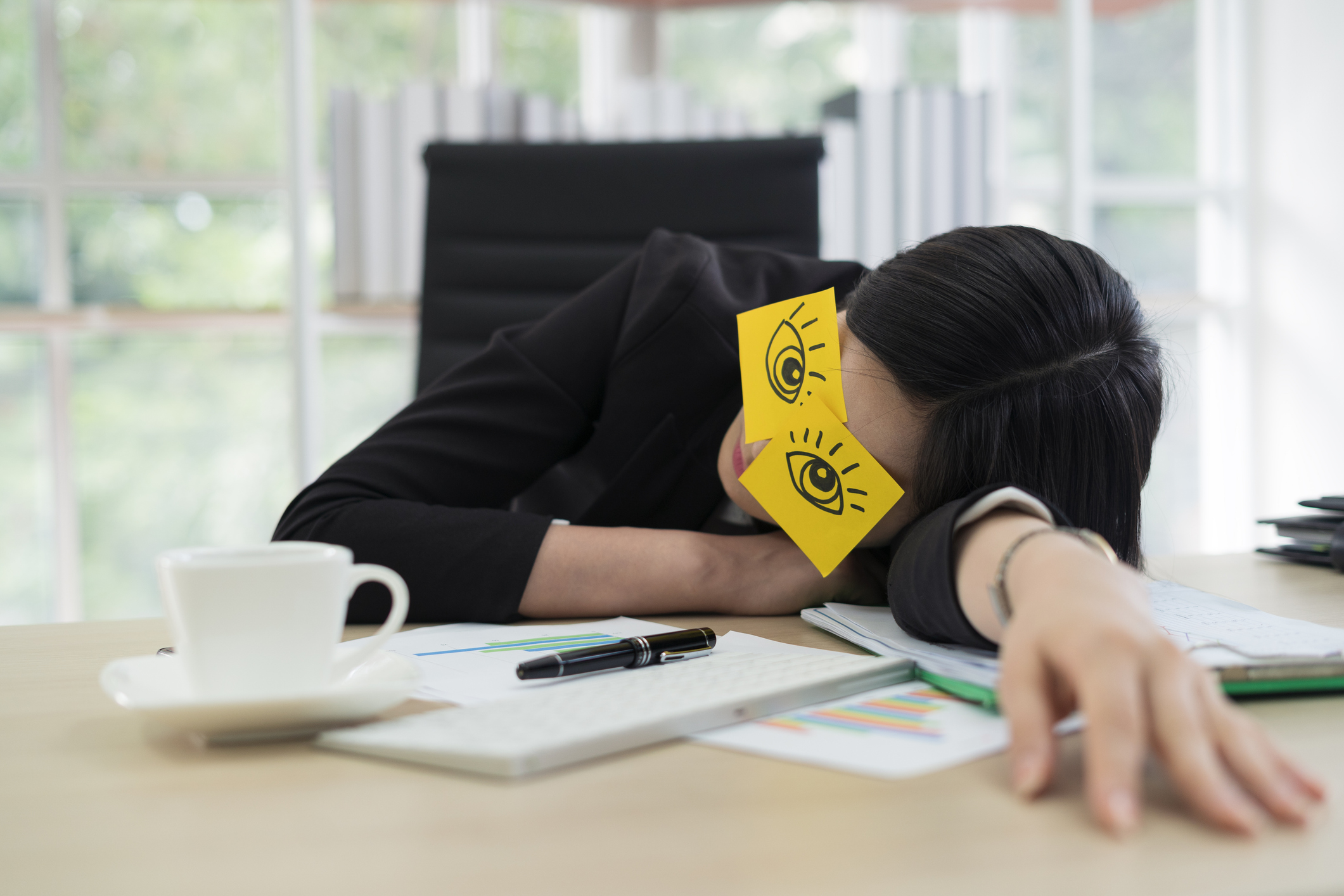 Young business woman with fake eyes painted on adhesive note sleeping at workplace in office (Getty Images/thianchai sitthikongsak)