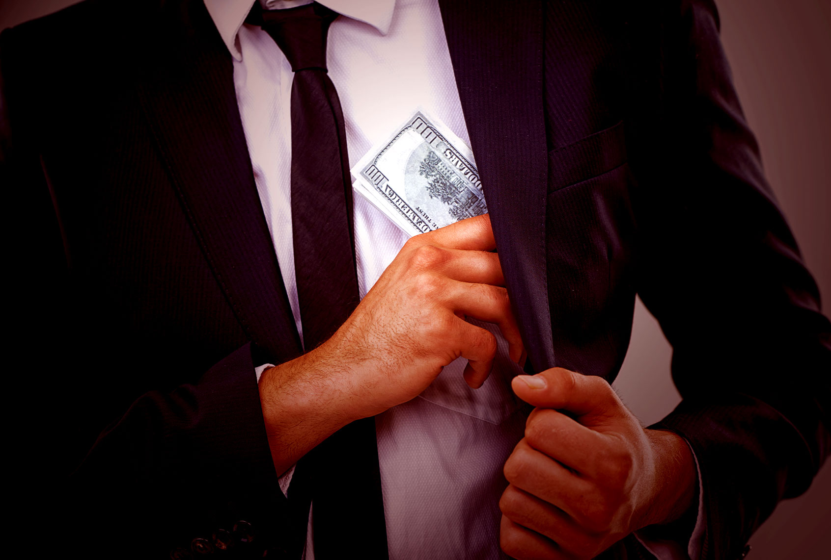Cropped image of a businessman putting money in his pocket (Getty Images)