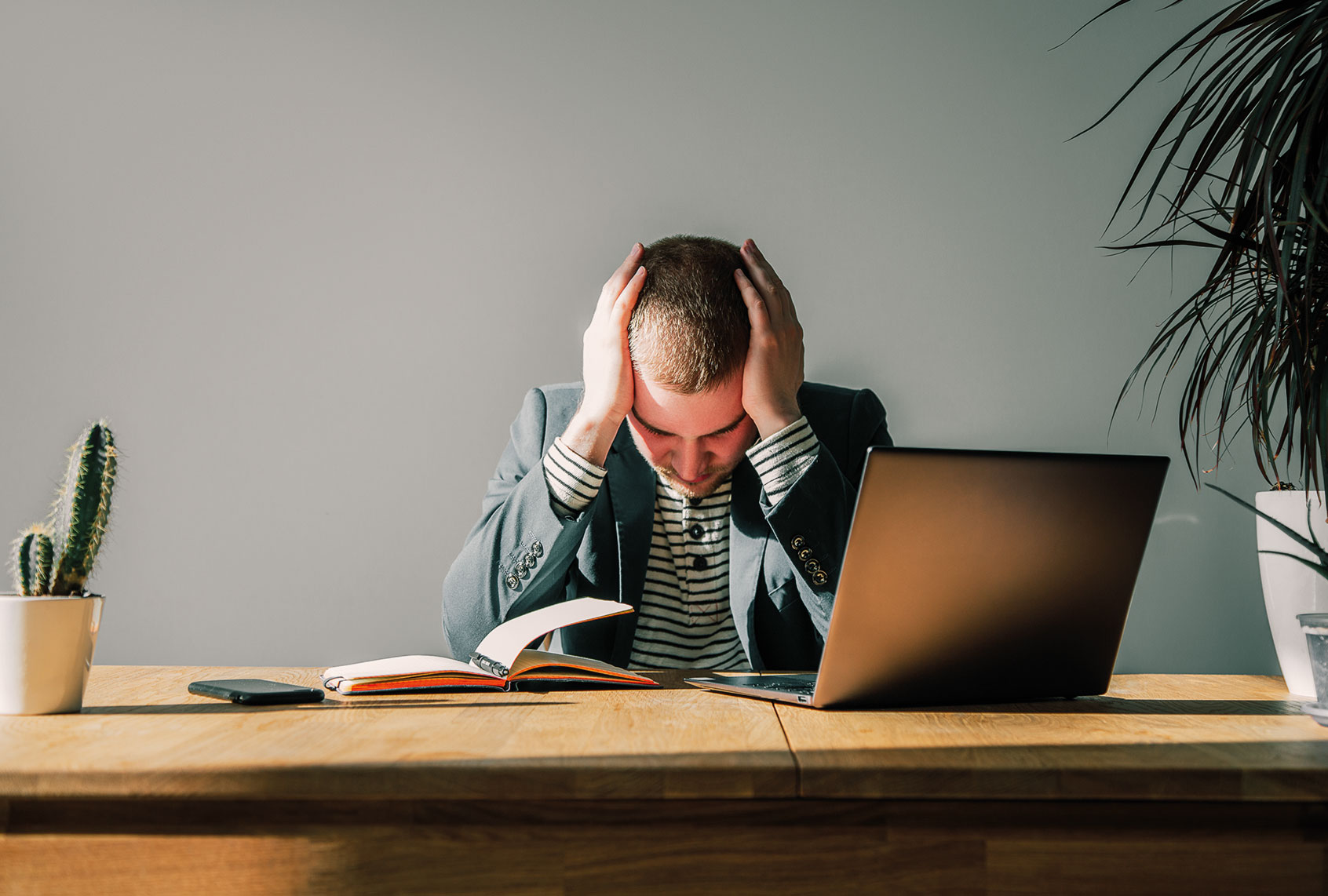 Worried businessman in dark suit sitting at office desk with laptop and notepad being overloaded with work. (Getty Images/Iuliia Bondar)