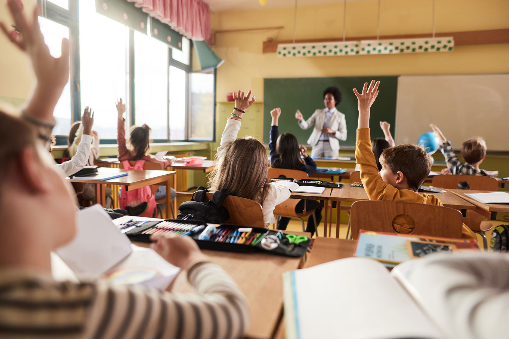 Large group of school kids raising their hands to answer the teacher's question on a class at elementary school. (Getty Images/skynesher)