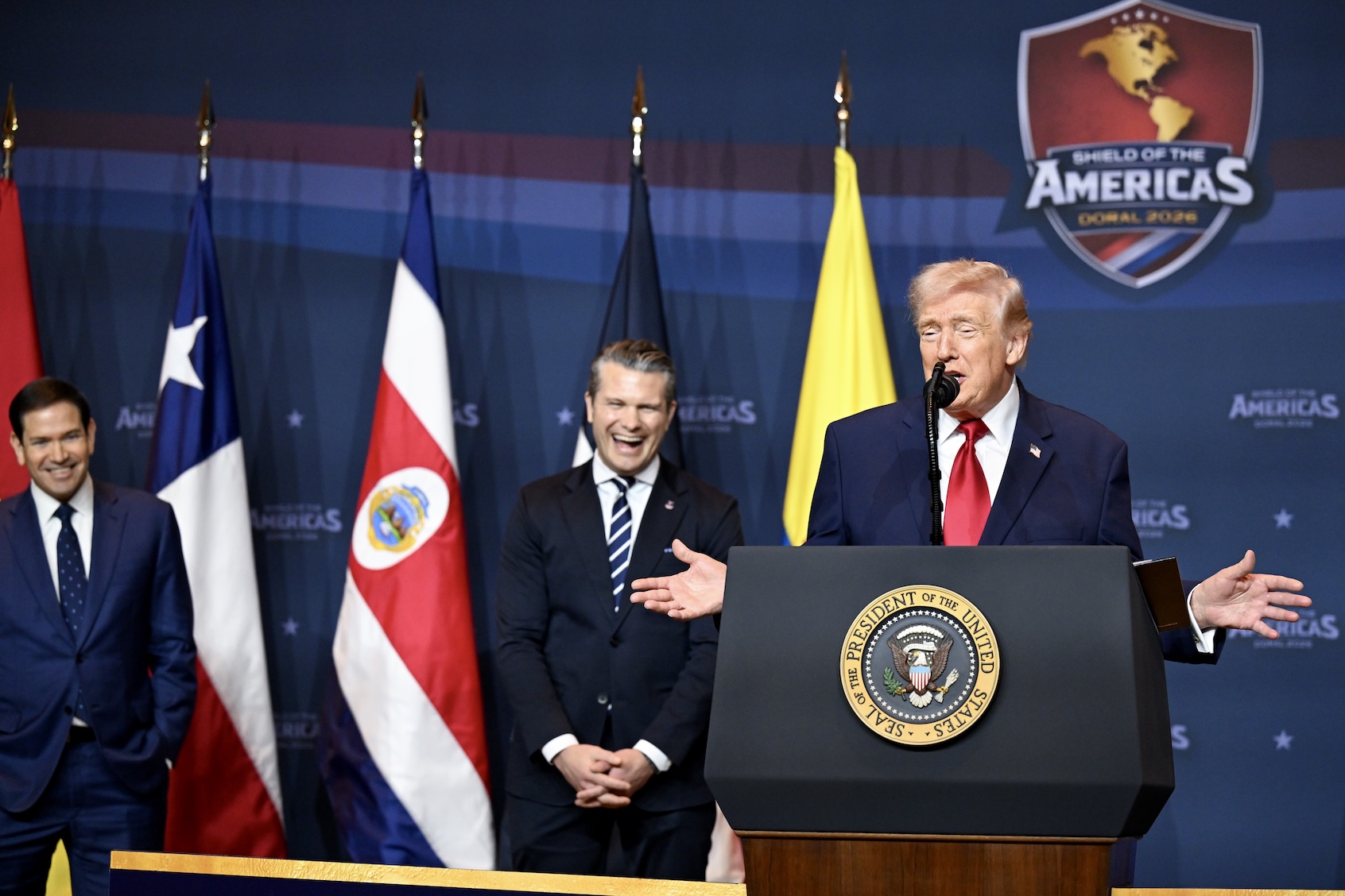 President Donald Trump speaks at âThe Shield of the Americas Summitâ as Secretary of State Marco Rubio (left) and Defense Secretary Pete Hegseth look on, Trump National Doral Golf Club, March 7, 2026. (Roberto Schmidt/Getty Images)