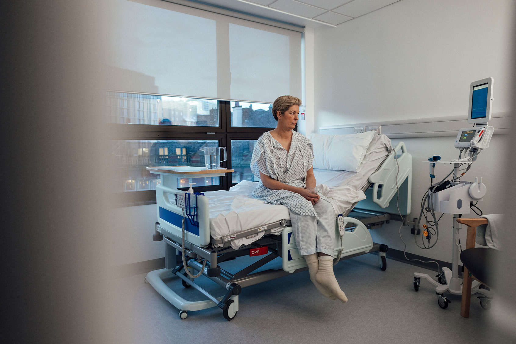 A woman sitting on the edge of her hospital bed before she goes for some treatment (Getty Images/SolStock)